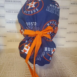 May include: A blue and orange surgical scrub hat with the Houston Astros logo. The hat has a tie on the back.