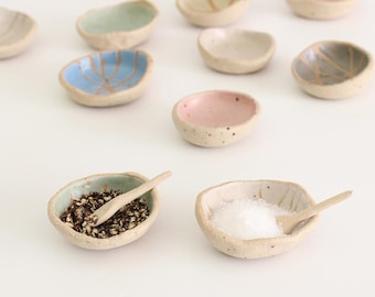 Può includere: Un set di dieci piccole ciotole in ceramica di vari colori, tra cui blu, verde, rosa e bianco. Ogni ciotola ha un design unico ed è perfetta per servire spezie, salse o condimenti.