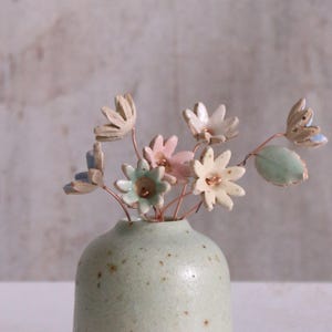 Peut inclure: Un petit vase en céramique vert moucheté avec un bouquet de fleurs en céramique pastel. Les fleurs sont dans des tons de rose, bleu et vert.