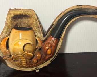 May include: A carved wooden pipe with a brown and black stem, in a leather case with a carved wooden design.