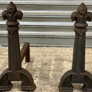 Peut inclure: Une paire de chenets en fonte avec un motif de fleur de lys sur le dessus. Les chenets sont noirs et ont une finition rustique.