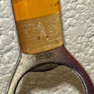 May include: Close-up of a vintage bottle opener with a silver-colored metal handle and a yellow-orange top. The word "FOREIGN" is stamped on the handle. The opener is likely used for opening bottles.