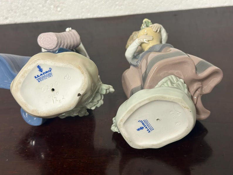May include: Two porcelain figurines, one in blue and white and the other in pink and white, with the Lladro logo on the bottom of each.