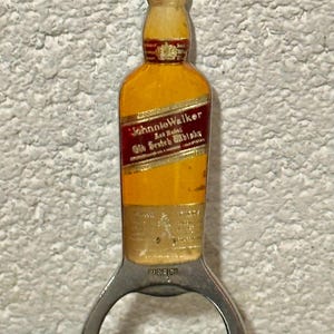 May include: Bottle opener shaped like a Johnnie Walker Scotch whisky bottle. The opener is yellow and red with the brand name and text. The bottom part is a silver bottle opener with the word "FOREIGN" printed on it.