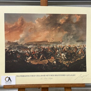 May include: A vintage print depicting a dramatic scene of the Charge of the British Cavalry at the Battle of Waterloo. The print is framed and features a signature in the bottom right corner.