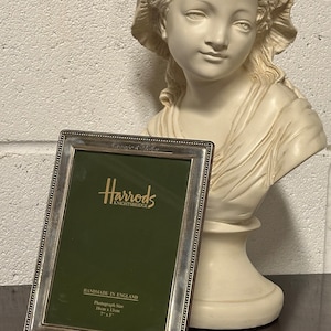 May include: A silver picture frame with a green mount and the Harrods Knightsbridge logo. The frame is handmade in England and has a photograph size of 18cm x 13cm.