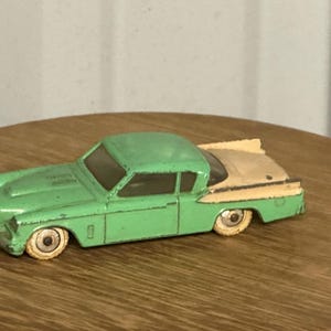 Könnte beinhalten: Ein altes Spielzeugauto aus Druckguss mit einer zweifarbigen Lackierung in Minzgrün und einem cremefarbenen Heck. Das Fahrzeug hat eine Coupé-Silhouette, klare Fenster und kleine weiße Räder. Der Lack weist deutliche Gebrauchsspuren auf.