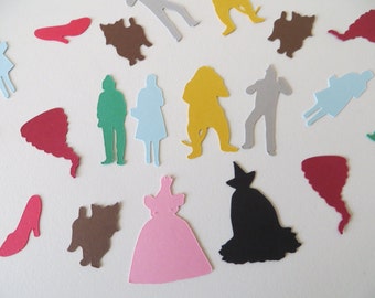 May include: A set of paper cutouts featuring characters from the Wizard of Oz. The characters include Dorothy, the Scarecrow, the Tin Man, the Cowardly Lion, the Wicked Witch of the West, and Toto. The cutouts are in various colors, including red, blue, green, yellow, and black.