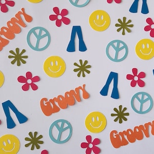 May include: A collection of colorful paper cutouts with a groovy theme. The cutouts include peace signs, smiley faces, flowers, bell bottoms, and the word "groovy" in a retro font.