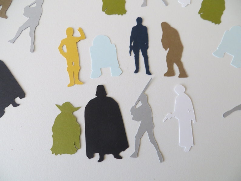 May include: A collection of paper cutouts of Star Wars characters, including Darth Vader, Yoda, R2-D2, and Chewbacca. The cutouts are in various colors, including black, green, blue, and brown.