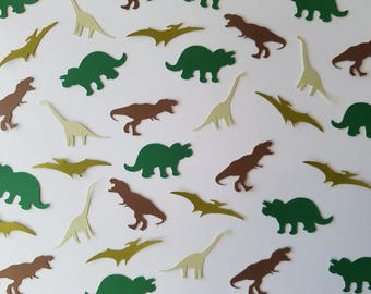 May include: Green, brown, and beige paper dinosaur cutouts on a white background. The dinosaurs include a triceratops, a stegosaurus, and a tyrannosaurus rex.