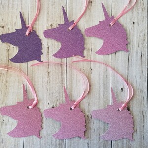 K&ouml;nnte beinhalten: Sechs Geschenkanh&auml;nger in Form eines Einhorns mit pinkfarbenem und violettem Glitzerfinish. Jeder Anh&auml;nger hat oben ein Loch f&uuml;r eine Schnur oder ein Band.