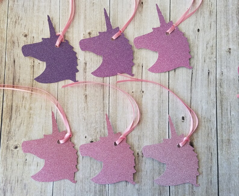 K&ouml;nnte beinhalten: Sechs Geschenkanh&auml;nger in Form eines Einhorns mit pinkfarbenem und violettem Glitzerfinish. Jeder Anh&auml;nger hat oben ein Loch f&uuml;r eine Schnur oder ein Band.