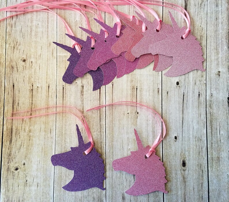 K&ouml;nnte beinhalten: Ein Satz von acht rosa und violetten Glitzer-Einhornkopf-Ausschnitten mit rosa Schleife. Die Einhornk&ouml;pfe sind in verschiedenen Rosat&ouml;nen und Violett.