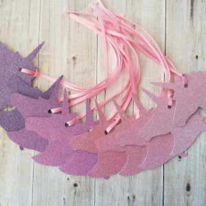 K&ouml;nnte beinhalten: Ein Set mit zehn pinkfarbenen und violetten Glitzer-Einhornkopf-Geschenk-Etiketten mit pinkfarbenem Satinband.