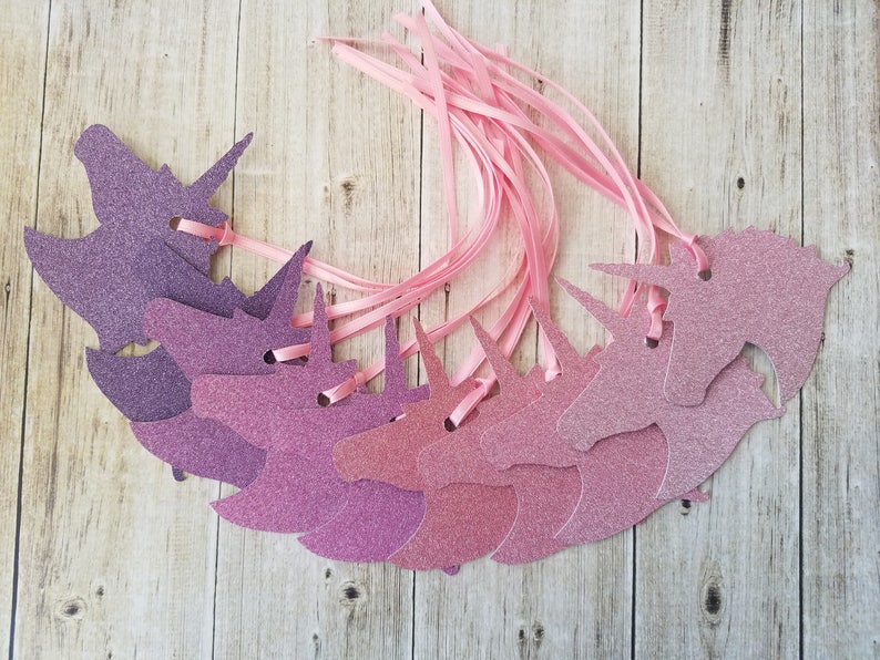 K&ouml;nnte beinhalten: Ein Set mit zehn pinkfarbenen und violetten Glitzer-Einhornkopf-Geschenk-Etiketten mit pinkfarbenem Satinband.
