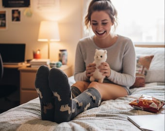 Puede incluir: Una persona con calcetines grises con un estampado de llama blanco y beige, sentada en una cama. La persona sostiene un peluche de llama blanco. Una bolsa de patatas fritas y un portátil están en la cama.