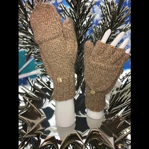 Puede incluir: Un par de guantes sin dedos de punto marrón con un detalle de botón marrón. Los guantes se muestran en una mano de maniquí.