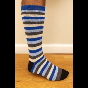 May include: Knee-high sock with horizontal stripes in blue, gray, and white. The toe and heel are black. The sock is on a wooden surface.