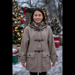 May include: A light brown duffel coat with a hood, toggle closures, and two front pockets. The coat is worn by a person standing in front of Christmas trees with lights and snow on the ground.