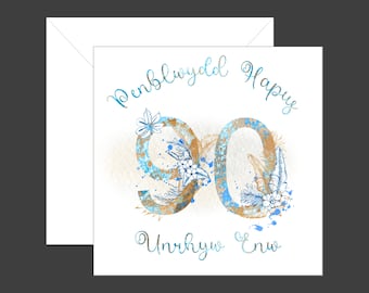 May include: A white card with a blue and gold 90 surrounded by floral designs. The text "Penblwydd Hapus 90 Unrhyw  Eni" is written in cursive on the card.