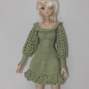 May include: A green crocheted dress with long sleeves and a ruffled hem. The dress is made with a delicate stitch pattern and has a vintage style.