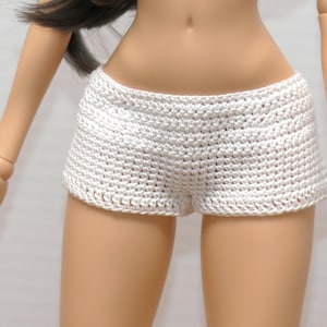 Op de afbeelding: Witte gehaakte shorts. De shorts zijn gemaakt van een strak geweven, getextureerd materiaal. Het kledingstuk is ontworpen met een lage taille en een eenvoudige, klassieke stijl. De shorts worden op een pop getoond.