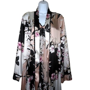 Pode incluir: Robe com estampa floral em tons de preto, branco e blush. O robe apresenta decote em V, mangas compridas e tecido acetinado. O padrão floral inclui flores rosa e folhas pretas.