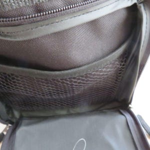 May include: Open view of a black travel bag interior. The bag features multiple compartments, including a mesh pocket and a zippered section. The interior is made of a durable, dark fabric, with a zipper closure at the top.