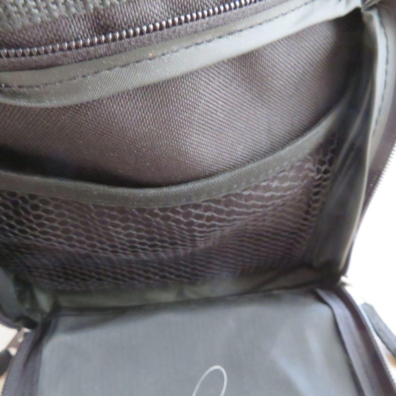 May include: Open view of a black travel bag interior. The bag features multiple compartments, including a mesh pocket and a zippered section. The interior is made of a durable, dark fabric, with a zipper closure at the top.