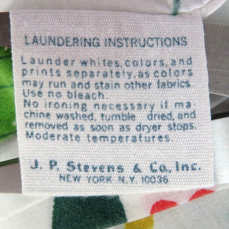 Puede incluir: Una etiqueta de tela blanca con texto azul que detalla las instrucciones de lavado. La etiqueta dice "Lavar blancos, colores e impresiones por separado...No usar lej&iacute;a..." e incluye el nombre de la empresa J.P. Stevens & Co., Inc., Nueva York, NY.
