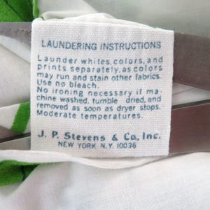 Puede incluir: Una etiqueta de tela blanca con texto azul que detalla las instrucciones de lavado. La etiqueta aconseja lavar blancos, colores y estampados por separado. Tambi&eacute;n incluye el nombre de la empresa J.P. Stevens & Co., Inc., Nueva York, N.Y. 10036.