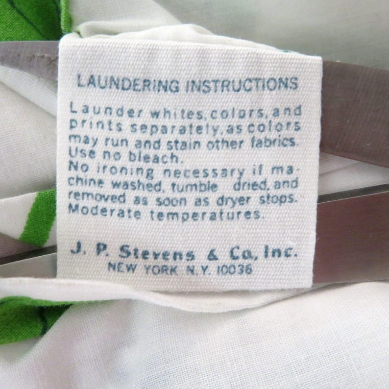 Puede incluir: Una etiqueta de tela blanca con texto azul que detalla las instrucciones de lavado. La etiqueta aconseja lavar blancos, colores y estampados por separado. Tambi&eacute;n incluye el nombre de la empresa J.P. Stevens & Co., Inc., Nueva York, N.Y. 10036.