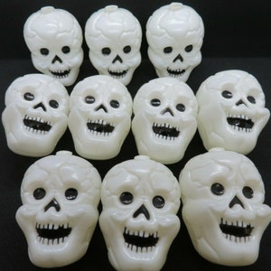 May include: Ten white plastic Halloween skull decorations with black eyes and mouths. The skulls are all facing forward and have a slightly grinning expression.