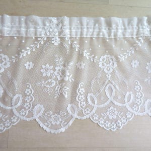 May include: White lace curtain panel with floral and leaf patterns. The lace features a scalloped bottom edge and a dotted top section. The design includes detailed floral motifs and delicate openwork, creating a vintage aesthetic.