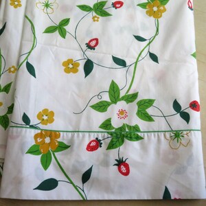 Puede incluir: S&aacute;bana blanca con un estampado repetido de vides verdes, flores amarillas, flores blancas y fresas rojas. La s&aacute;bana tiene un borde verde a lo largo del borde inferior.