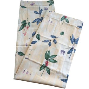 May include: Two cream-colored fabric panels with a floral pattern. The design features green leaves, blue leaves, and pink berries. The background has a subtle, light yellow grid pattern.