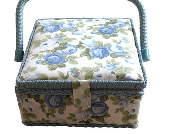 May include: A blue wicker sewing box with a floral patterned lid and a padded cushion top. The box has a handle and a hinged lid.