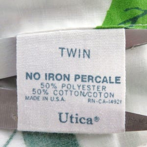 Puede incluir: Una etiqueta de tela blanca con la palabra "TWIN" en la parte superior. Debajo, indica "NO IRON PERCALE" y detalla la composici&oacute;n de la tela: 50% poli&eacute;ster y 50% algod&oacute;n. La etiqueta est&aacute; marcada "MADE IN U.S.A." e incluye la marca "Utica&reg;".