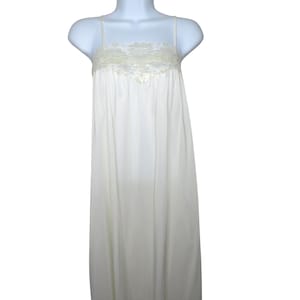 May include: Ivory-colored slip dress with spaghetti straps. The bodice features a delicate lace trim along the neckline. The dress has a flowing, floor-length design, creating a classic and elegant silhouette. The fabric appears to be lightweight and smooth.