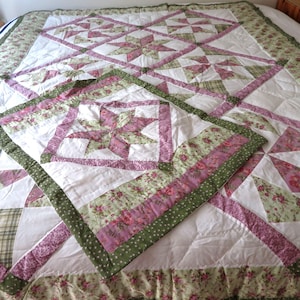 Peut inclure: Un couvre-lit en patchwork et sa taie d'oreiller assortie présentant un motif en étoile dans des tons rose, blanc et vert sauge. Le tissu comprend des imprimés floraux, des carreaux et des pois, avec un bord à volants sur le couvre-lit.