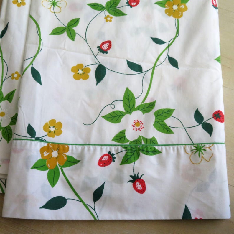 Puede incluir: S&aacute;bana blanca con un estampado repetido de vides verdes, hojas, flores amarillas, flores blancas y fresas rojas. La s&aacute;bana tiene un borde verde en el borde inferior. El tema general es un dise&ntilde;o floral y de frutas.