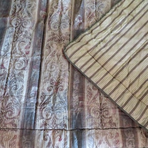 May include: A quilted bedspread and pillow sham set. The bedspread features vertical stripes with floral and scroll patterns in shades of gray, purple, and cream. The pillow sham has a striped pattern in similar colors.