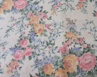 May include: A white fabric with a floral pattern featuring pink, yellow, and blue flowers. The fabric has a pink trim around the edge.
