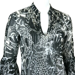 May include: A black and white sheer blouse with a floral print and a V-neck. The blouse has long sleeves with bell cuffs.