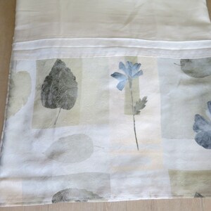 May include: White fabric with a subtle pattern of blue flowers and gray leaves. The fabric has a textured surface and a subtle sheen.