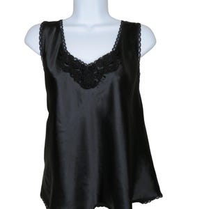 Puede incluir: Camisola de satén negro con ribete de encaje en el escote y el dobladillo. La parte superior sin mangas presenta un diseño de cuello en V con detalles de encaje en el centro. La tela tiene un brillo sutil y la prenda se muestra en un maniquí blanco.