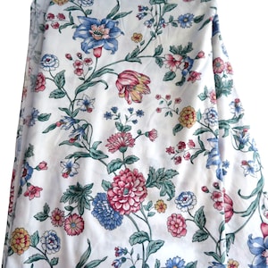 Puede incluir: Una tela blanca con un patrón floral repetitivo de grandes flores azules, rosas y amarillas conectadas por tallos y hojas verdes finas. El diseño incluye varios tipos de flores, como crisantemos y tulipanes, sobre la superficie.