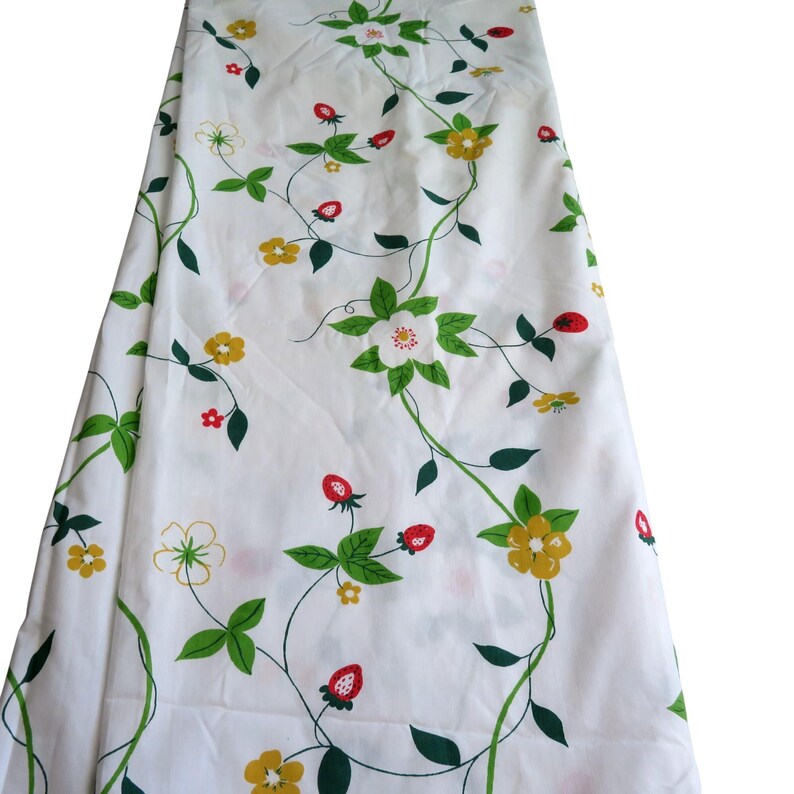 Puede incluir: Tela blanca con un patr&oacute;n repetido de vides verdes, flores amarillas y blancas y fresas rojas. La tela est&aacute; doblada, mostrando el patr&oacute;n en toda la superficie. El dise&ntilde;o es un estampado floral vintage.