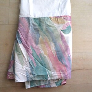 May include: A folded white and patterned textile. The pattern features streaks of pink, purple, green, and yellow on a white background. The textile appears to be a bed sheet or similar bedding item.
